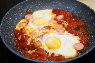 Fried eggs with tomatoes and chopped sausages. Hearty healthy quick breakfast. Home cooking food