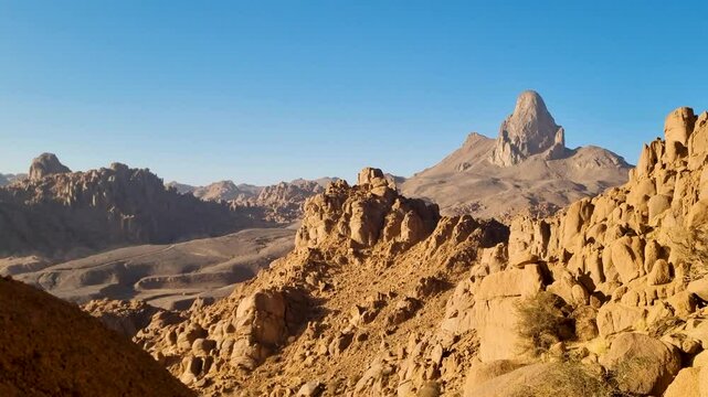 Rocky mountains in the Sahara desert in the Tamanrasset region of Algeria with holy Mount Ilamane during evening golden hour.