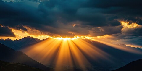 Sunset sunbeams shine through the mountains under a cloudy sky, creating a breathtaking scene. The setting sun illuminates the clouds, enhancing the beauty of the sunset in the mountains.