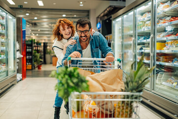 Happy couple having fun while shopping for groceries in supermarket