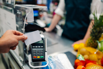 Customer paying with contactless credit card at supermarket checkout