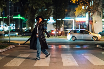 Stylish woman crossing the street at night in urban city