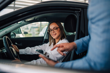 Woman smiles in car as salesman assists with digital interface.