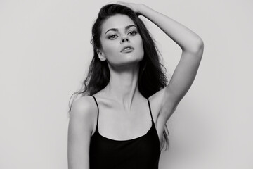 Fototapeta premium Elegant young woman posing confidently with one hand on her head, showcasing beauty and grace in a minimalist black and white setting. Fashion and portrait concept.