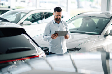 Car salesman in showroom checking details on tablet device