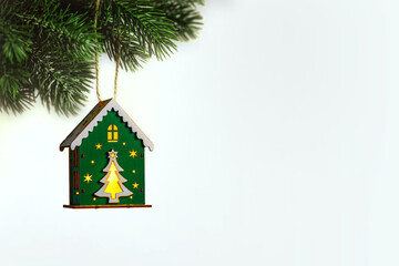 Christmas tree toy in the form of a house with glowing windows hanging from christmas tree branch,...