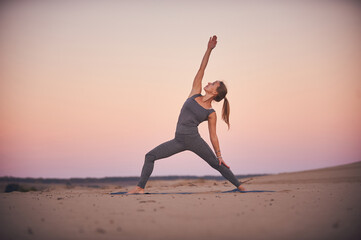 Fototapeta premium Practicing yoga at sunset on a sandy beach with a serene atmosphere