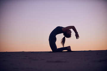 Woman practicing yoga in a sunset silhouette over a sandy landscape