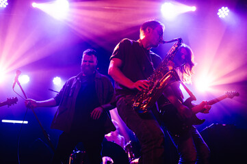 Musicians playing saxophone, guitar and singing during live concert under purple stage lights