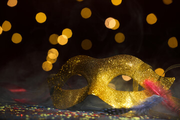Beautiful carnival mask and confetti in smoke on dark background with blurred lights, closeup