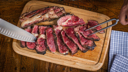 Top view of sliced rare cote de boeuf steak being prepared on wooden board with knife and meat serving fork on wooden table in restaurant