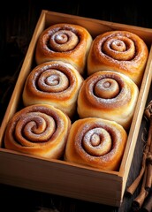 Fototapeta premium Wooden box with six cinnamon rolls inside. The rolls are sprinkled with powdered sugar. The box is placed on a wooden table