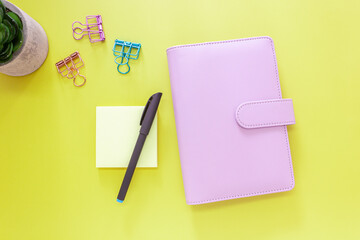 Pink Planner with Sticky Notes, Pen and Clips on Yellow Background
