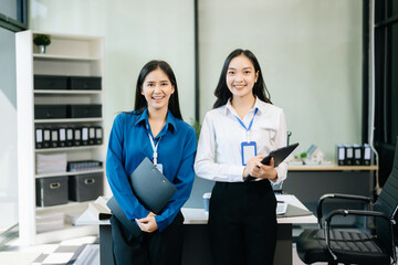 Fototapeta premium Professional women smiling confidently, collaborating with a tablet and clipboard in a modern office.