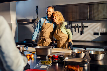 Middle-aged couple enjoying a cooking class with a chef preparing meal in the kitchen..