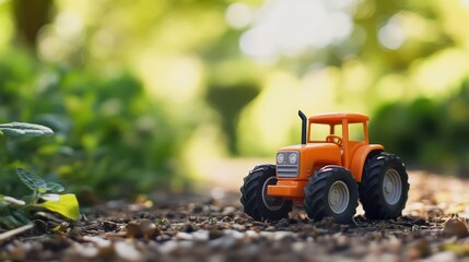 Bright orange toy tractor positioned on gravel path in a lush garden, surrounded by soft green foliage and a blurred natural backdrop.