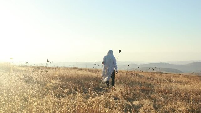 A jew prays in a field at sunrise, with tallit and Sidur. Tfilat Shacharit.