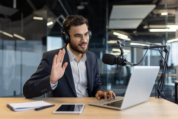 Man in office records podcast using microphone and laptop, wearing headphones. Engages audience...