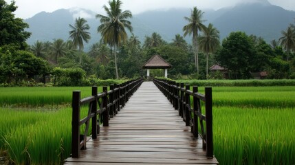 Obraz premium Serene Wooden Pathway through Lush Green Rice Fields with Majestic Mountains in the Background and Cloudy Sky