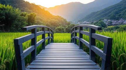 Obraz premium Scenic View of a Wooden Bridge over Lush Green Rice Fields at Sunset with Mountains in the Background Capturing Tranquility and Natural Beauty