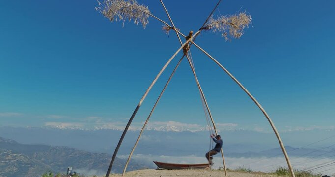 A Drone captures a local man enjoying the bamboo swing during Dashain Festival, set against a backdrop of mountain ranges, blue skies, and a scene of happiness, joy, and peace