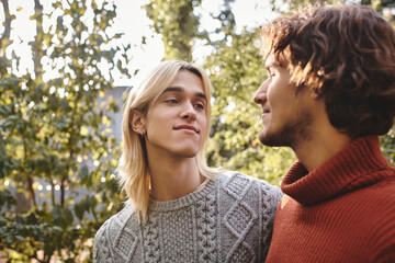 Fototapeta premium Two handsome young men share a heartfelt glance in a lush garden filled with greenery. They radiate joy and companionship, enjoying a beautiful day outdoors, surrounded by nature and warmth.