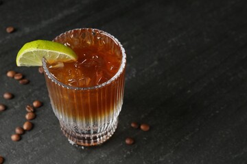Refreshing espresso tonic drink with slice of lime and coffee beans on dark table, closeup. Space...