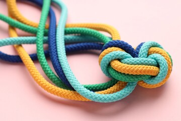 Colorful ropes tied in knot on light pink background, closeup. Unity concept