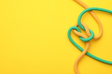 Colorful ropes tied in knot on yellow background, top view with space for text. Unity concept