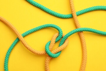 Obraz premium Colorful ropes tied in knot on yellow background, top view. Unity concept