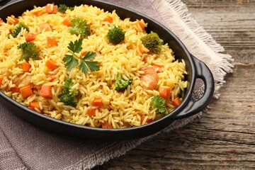 Tasty rice with vegetables in baking dish on wooden table, closeup