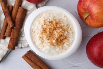 Delicious rice pudding with apples and cinnamon sticks on white textured table, flat lay