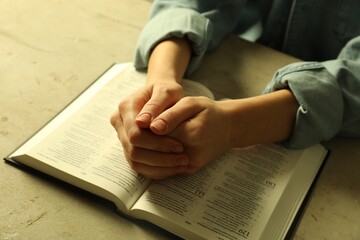 Naklejka premium Woman with open Holy Bible in English language praying at beige table, closeup