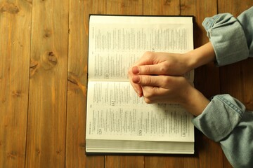 Woman with open Holy Bible in English language praying at wooden table, top view
