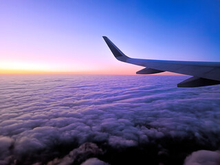 Obraz premium Wing of plane flying in sky above clouds at dawn. Travel, transport concept