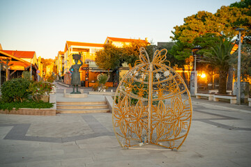 Christmas decorations on the square with bronze statue of a market woman in Novalja, island of Pag