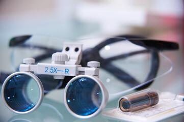 Close-up of dental or surgical loupes with magnifying lenses on a reflective surface. Professional medical equipment used for precision work.