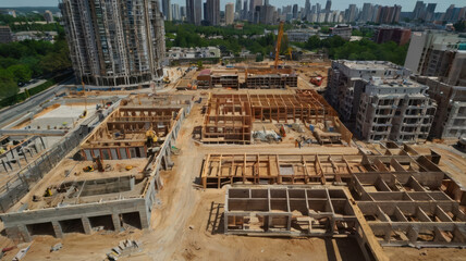Construction site with buildings under development, showcasing cranes and workers. urban landscape features mix of structures and greenery, highlighting ongoing development