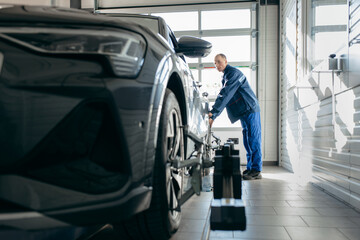 Auto mechanic installing sensor during suspension adjustment and automobile wheel alignment work at repair service station