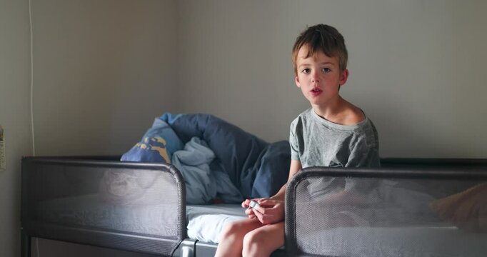 Young boy sits on a bunk bed and appears to be talking and gesturing with his hands