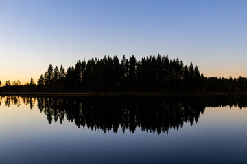 Fototapeta premium A peaceful sunset over a lake in Lapland, Sweden, with the reflection of trees in the still water.