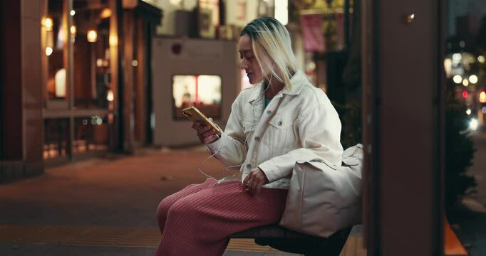 City, woman and night with smartphone for music, audio track and kpop playlist at bus stop. Japanese person, travel and mobile app with earphones for listening song, dancing and waiting for transport