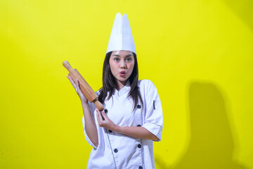 An Asian female chef wearing a white chef uniform and tall chef hat, smiling confidently while...