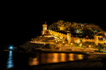 Beautiful Tossa de Mar Mediterranean town by night. Illuminated medieval fortress and city walls by the sea. Beach, pine trees and light reflections. Costa Brava, Catalonia, Spain