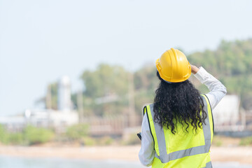 female engineer with hardhat with petrochemical factory background. asian woman holding tablet, plan and Walkie Talkie.