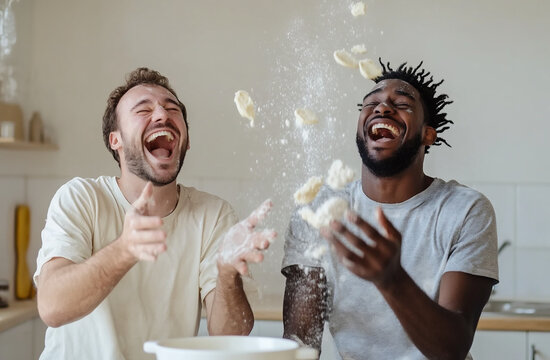 A pair of men, one Latino and one African-American, having a pancake-making competition in their bright kitchen. Pancakes are flying in the air, and flour is scattered everywhere, while they laugh hys