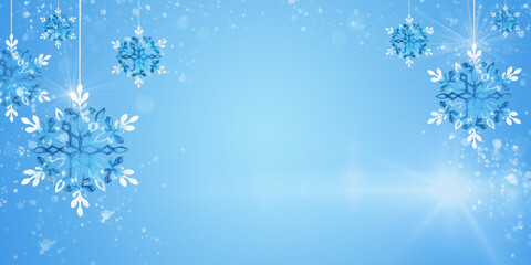 Christmas ornaments blue snowflakes hanging with sun glare and flying snow on blue background, copy space. Banner, website header, poster with cope space.