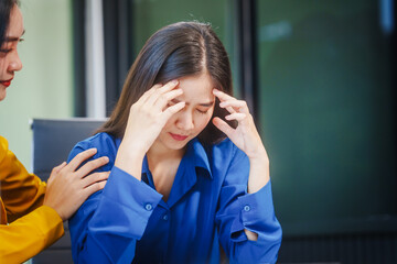 Two young Asian businesswomen, colleagues and friends, work at desk indoor office, analyzing financial charts on desktop, laptop, and tablet, facing stress and discussing solutions to avoid failure.