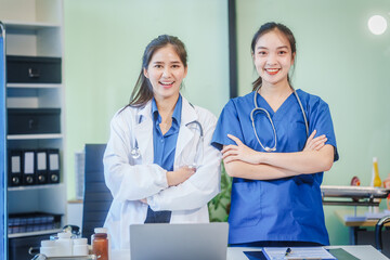 Two Asian girls, a doctor and a nurse assistant, work together at a desk in a hospital, analyzing...