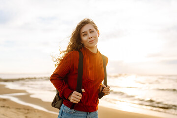 Portrait of a beautiful woman on the beach at sunset. Cold weather.  Tourist, active lifestyle, relax concept.